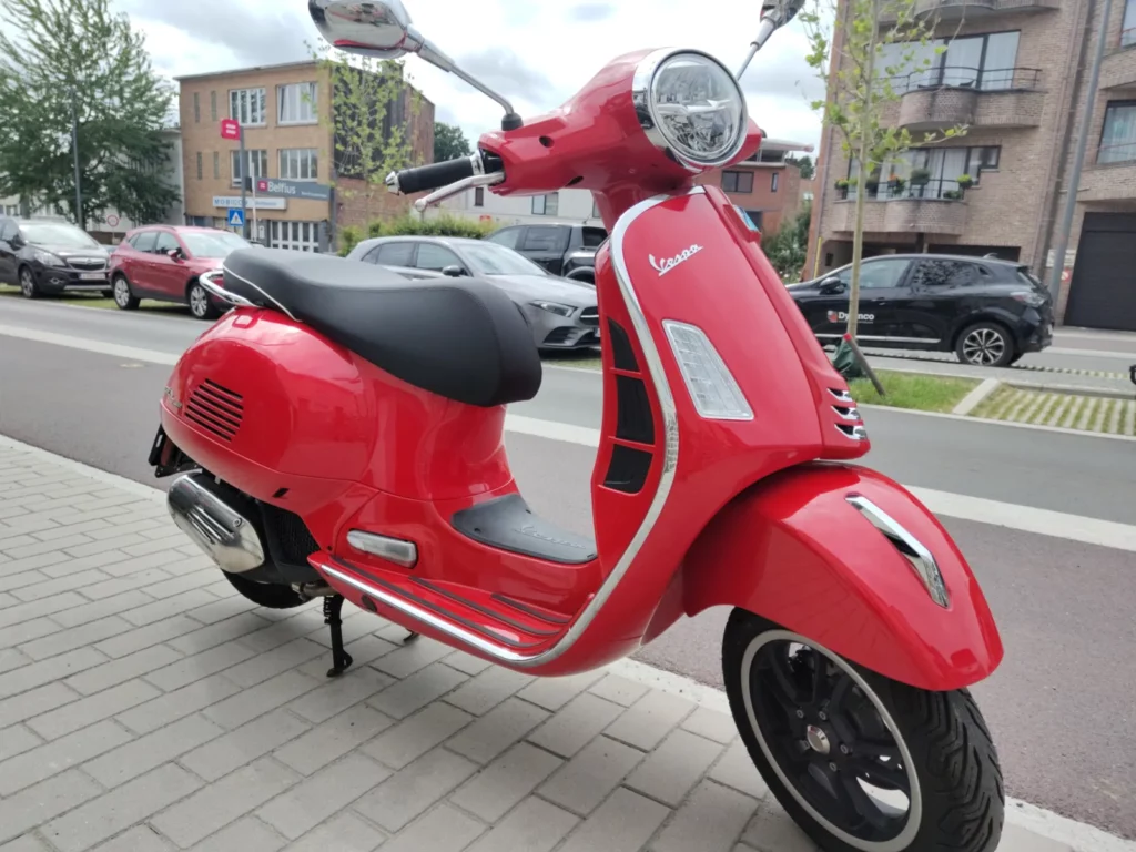Vespa GT Super 125 cc, 2023 côté droit sur le chevalet central. Moto rouge avec les chromes et la selle noire. Vespa d’occasion Gianni Moto