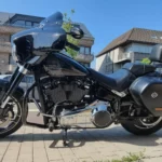Profil complet du côté gauche de la Harley-Davidson Sport Glide 2018 noire, montrant la béquille, la selle biplace avec repose-dos passager et la sacoche latérale.
