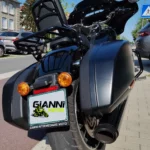 Vue arrière de la moto montrant le large pneu arrière, le porte-bagages avec sissy bar, les clignotants orange et la plaque d'immatriculation personnalisée au logo GIANNI MOTO.