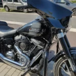 Gros plan sur le réservoir noir avec logo Harley-Davidson gris et le grand carénage avant de style Batwing, montrant le filtre à air performance et la barre de protection moteur.