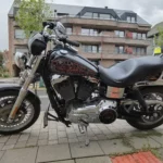 Profil latéral gauche d'une Harley-Davidson Dyna Low Rider noire garée sur le trottoir, avec dosseret sissy bar et détails chromés.