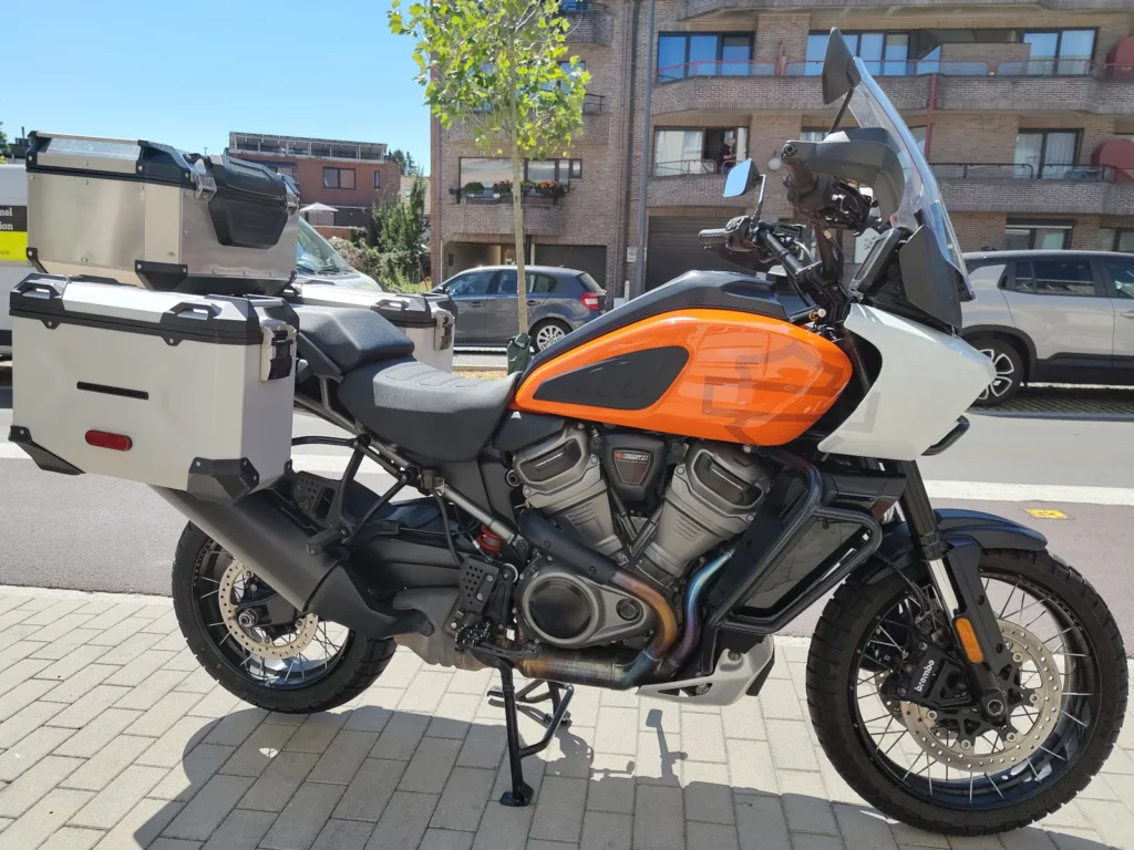 Vue latérale droite d'une Harley-Davidson Pan America 1250 orange et blanche équipée de valises rigides et d'un top-case en aluminium.