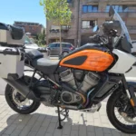 Vue latérale droite d'une Harley-Davidson Pan America 1250 orange et blanche équipée de valises rigides et d'un top-case en aluminium.