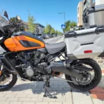 Profil latéral gauche d'une Harley-Davidson Pan America 1250 orange et blanche garée sur béquille centrale.